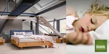 Bett mit Holzgestell im hellen Schlafzimmer mit Dachschrägen und schlafendes Kind auf dormiente-Kissen